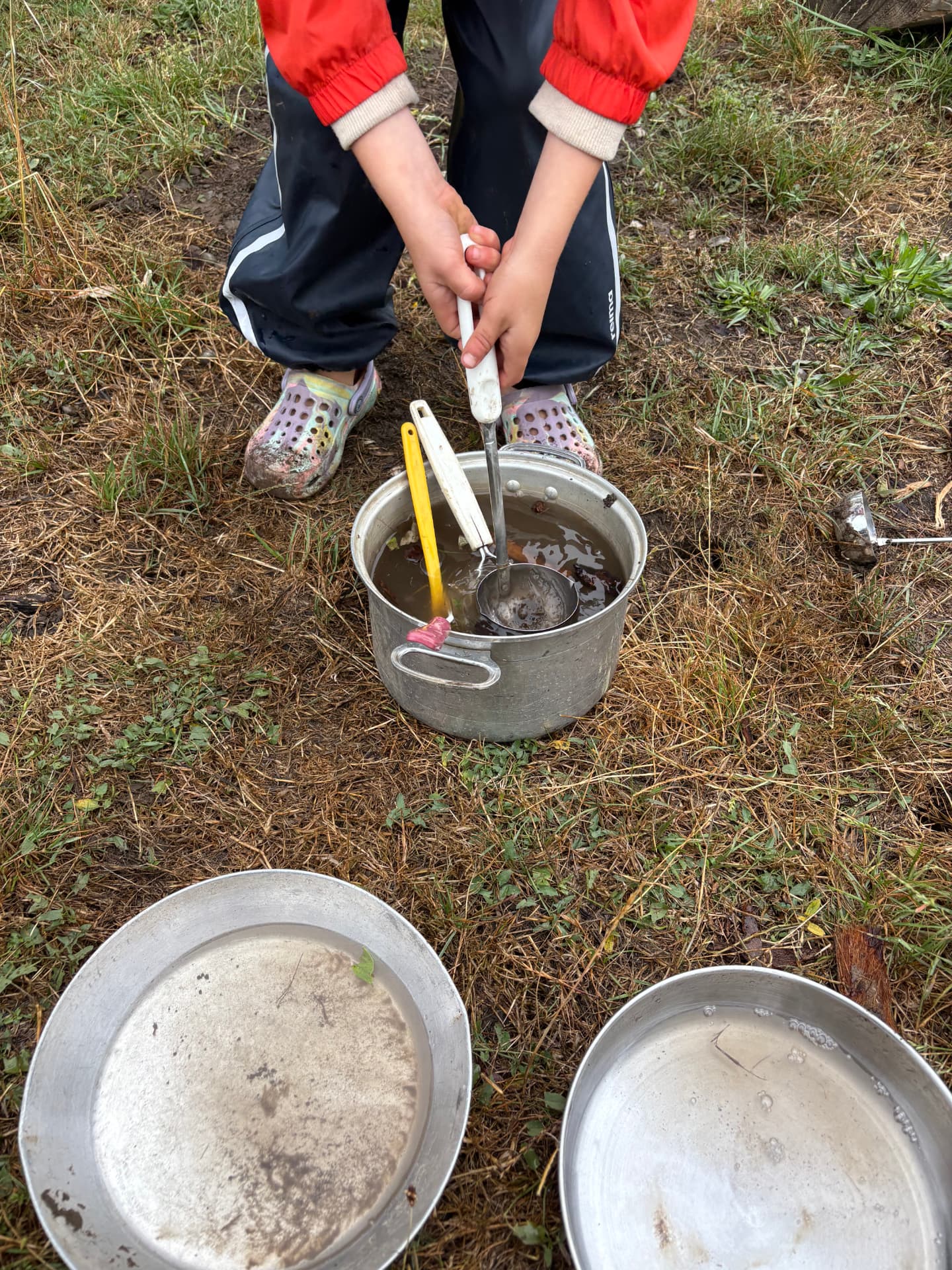 Small hands stirring a pot of mud soup in the outdoor kitchen